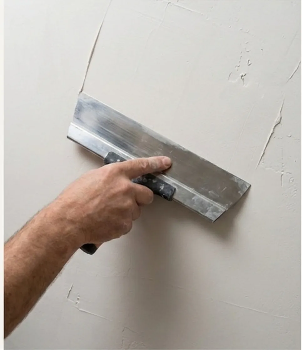 Plasterer applying a Level 5 skim coat to a wall with a broad plastering knife
